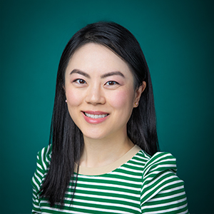 Female trauma surgeon smiling in front of teal photo backdrop.